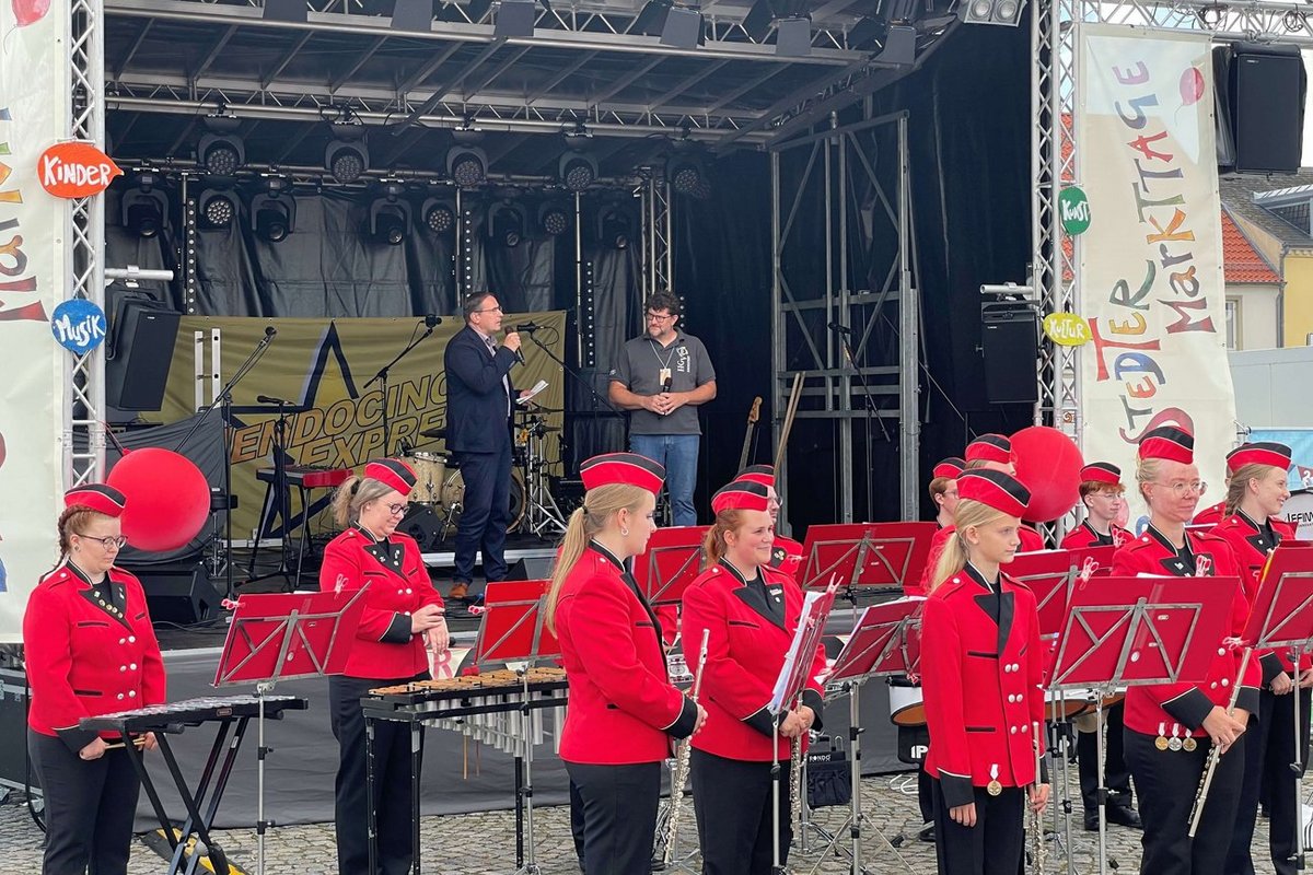 Die Eröffnung am Donnerstag mit Bürgermeister Christian Schmidt, dem HGV Vorsitzenden Karsten Werner und dem Bredstedter Spielmannszug. Zwei Männer auf einer Bühne, davor stehen Musiker
