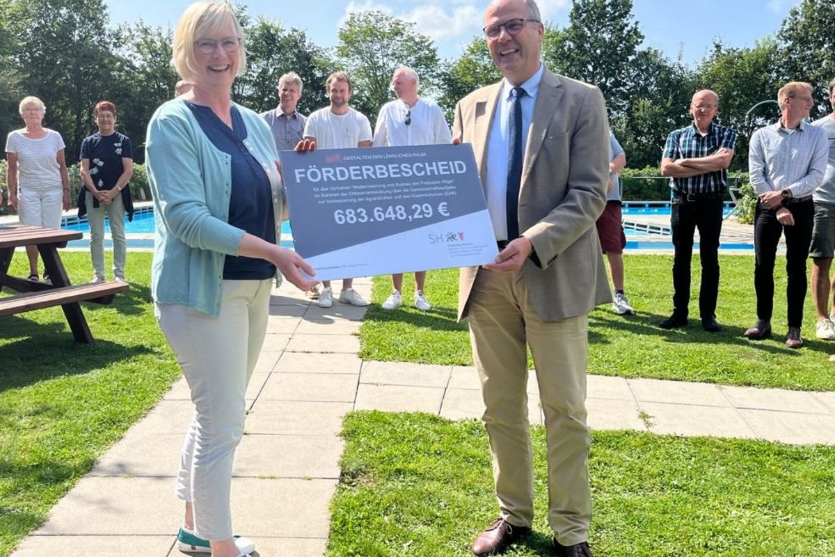 Minister Werner Schwarz überreicht Tanja Carstensen (Bürgermeisterin Högel) den Symbolischen Förderbescheid. Foto: MLLEV Eine Frau und ein Mann halten gemeinsam einen Scheck.