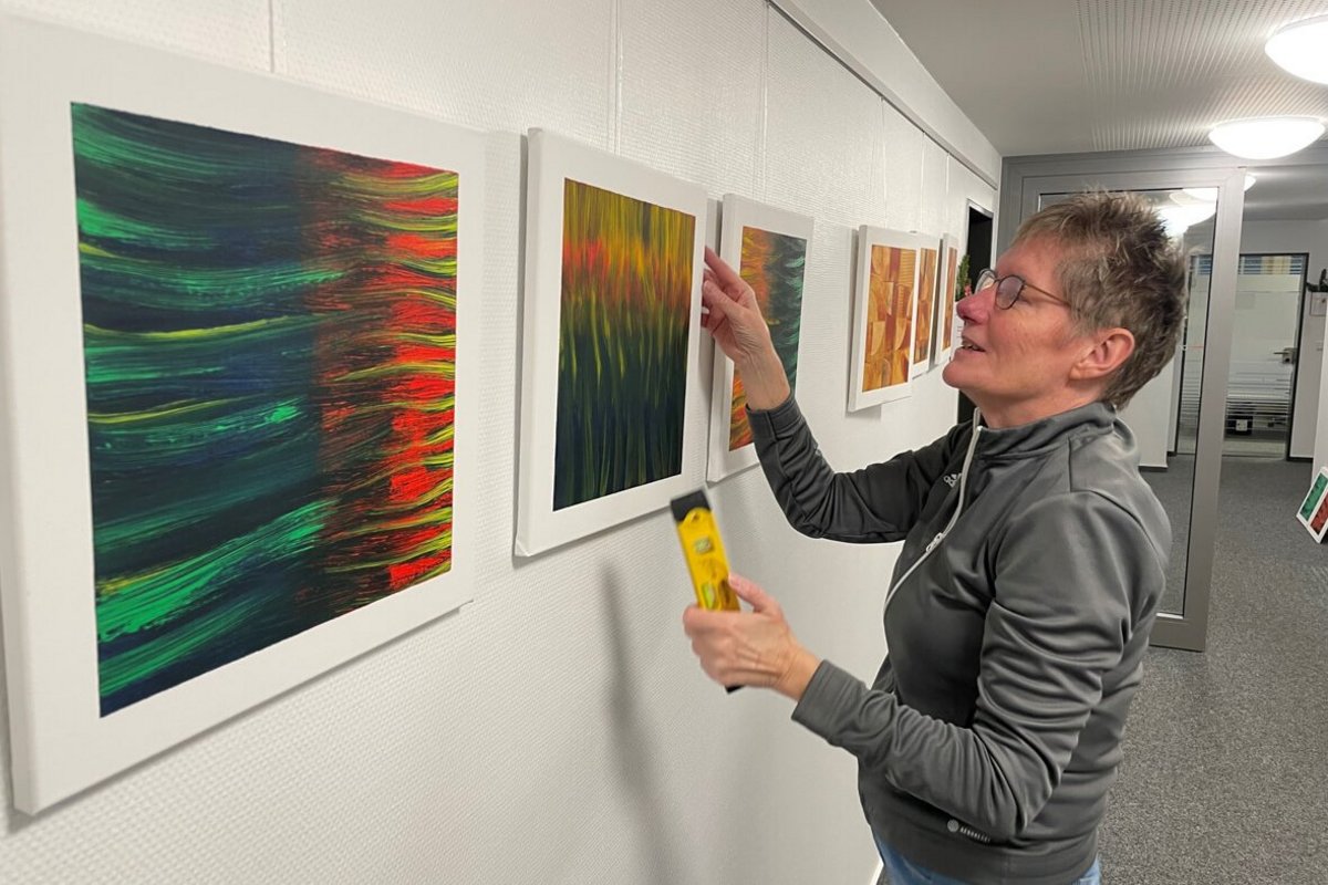 Susanne Weber zeigt abstrakte Acrylmalerei im Bredstedter Amtsgebäude. Foto: Felix Middendorf eine Frau hängt einen Bilderrahmen an eine Wand.