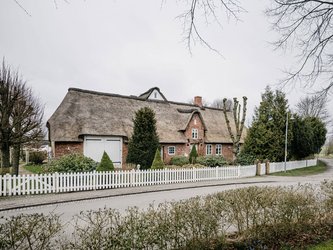 Haus mit Reetdach und weißem Zaun