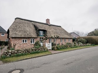 Haus mit Reetdach, Steinmauer und weißem Tor